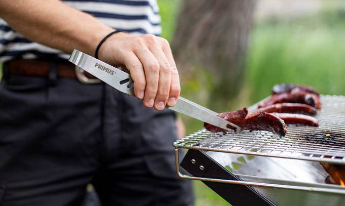 Eine Person hält eine Grillzange in der Hand und wendet damit etwas auf einem Grill